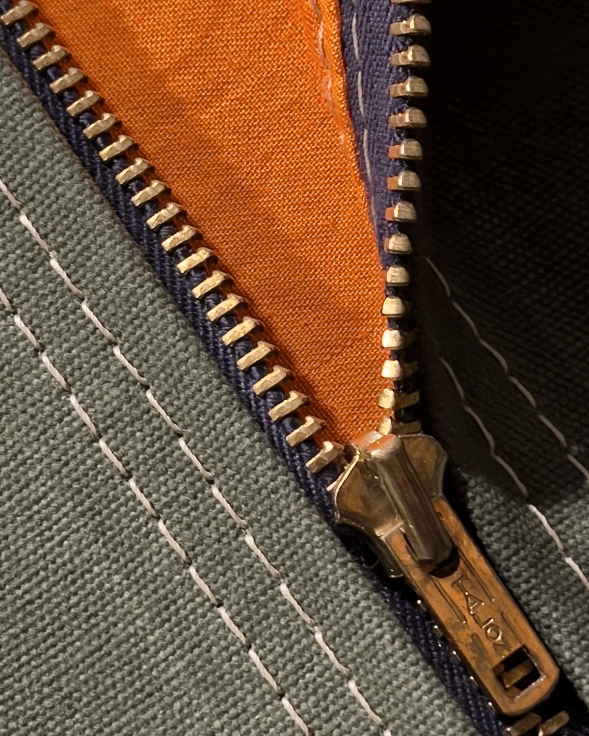 Vintage Talon brass zipper on waxed OD canvas, with the orange face of a Combat Identification Panel behind the teeth.